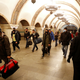 many people walk in an underground subway station corridor with arched walls and chandeliers hanging from the ceiling.